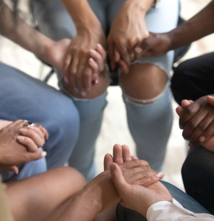 Close up vertical view diverse people sitting on chairs in circle hold hands, drug alcohol addiction rehab, support group counseling, therapy session, religious team, psychological help trust concept